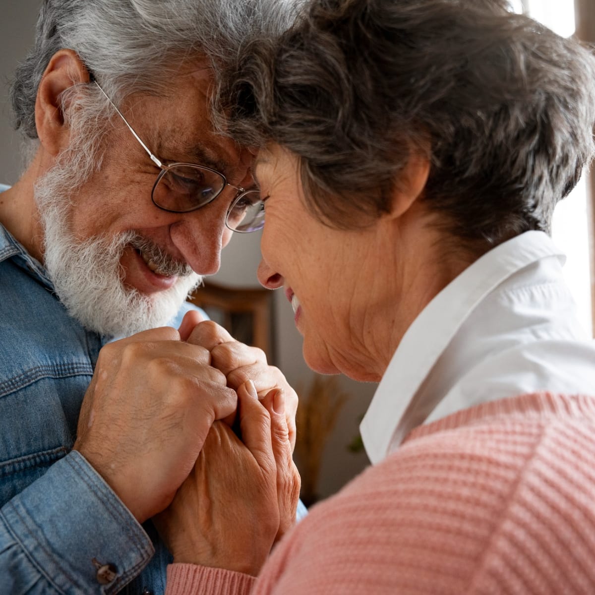 An elderly couple holding hands and resting their foreheads on each other