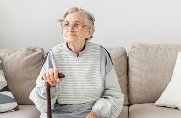 Old lady sitting on the couch holding her cane